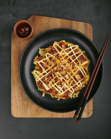 Japanese okonomiyaki pancake with mayo and bonito flakes on black plate, top viewの写真素材