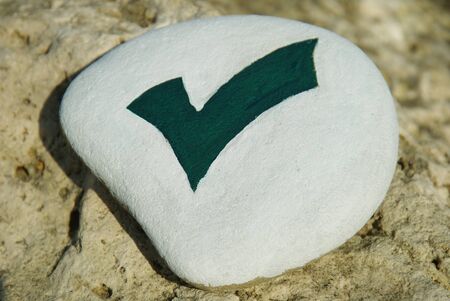 stone with design of green check mark isolated on white over a rockの写真素材