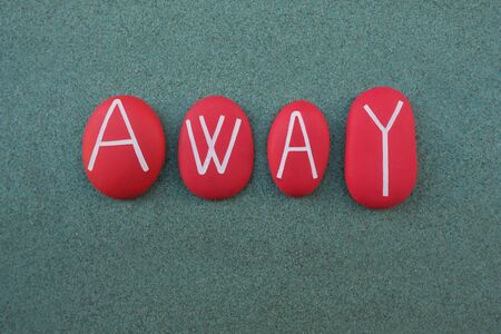 Away text composed with red colored stone letters over green sandの写真素材