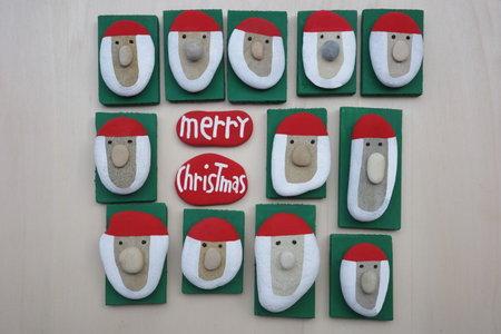 Merry Christmas message composed with handmade Santa Claus heads with colored stones and pebbles on...