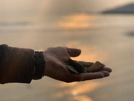 Man holding stones at beach during sunsetの写真素材