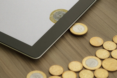 Golden coins scattered over the table turn into digital money through an electronic device. Conceptual image for digital economy, financial eletronic transactions, software for economics and accounting, investment in technology and innovation, money savinの写真素材