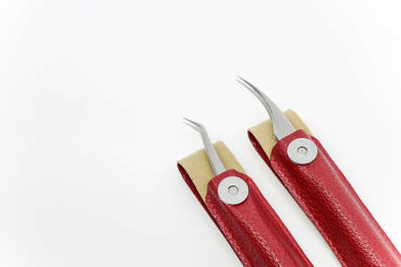 Straight and curved eyelash extension tweezers in red leather case with magnetic button on top of a white background.の写真素材