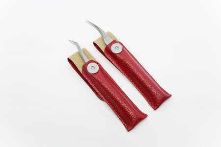 Straight and curved eyelash extension tweezers in red leather case with magnetic button on top of a white background.の写真素材
