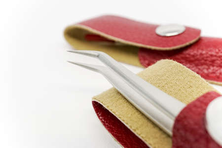 Close up shot of a curved eyelash extension tweezers in a red leather case with magnetic button on top of a white background.の写真素材