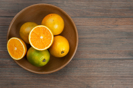 Oranges, vitamin C, in a clay bowl, brown.A half cut orange.Autumn wood color background.View from...