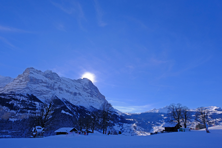 The sun hides behind the famous peak of the Eiger mountain above Grindelwald, with a lot of snow in winter season, Bern, Switzerland, Europeの写真素材