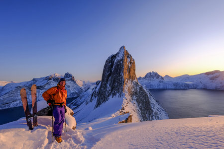 Skitouring man standing at the ridge in front of the iconic Segla mountain, view of the ocean...