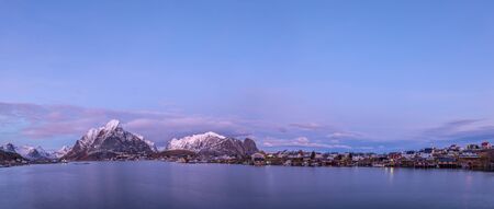 Wide panorama of Reine, with the snow covered mountains in the background and the famous fishing cabins Rorbu in the foreground, Lofoten Islands, Moskenesoya, Nordland, Norway, Europeの写真素材