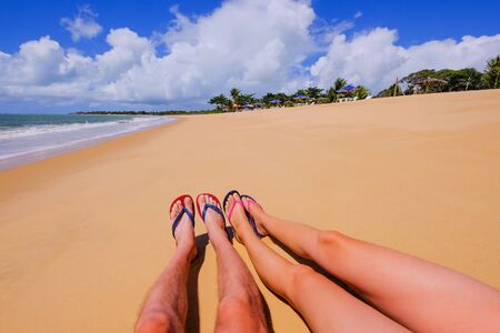 The beautiful naked legs of a young couple wearing flip flops on the sandy beach Praia Do Mutari Brava, Santa Cruz Cabralia, Coroa Vermelha, Porto Seguro, Bahia, Brazil, South Americaの写真素材