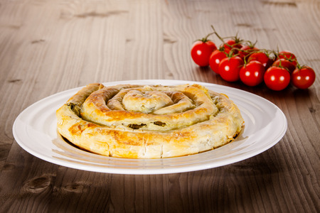 Spinach and cheese pie on white plate with tomatoes in backgroundの写真素材