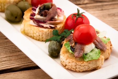 Crostini vith mozzarella cheese anchowy and tomato on wooden boardの写真素材