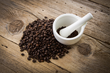 Coffee beans on rustic wooden background and white mortarの写真素材