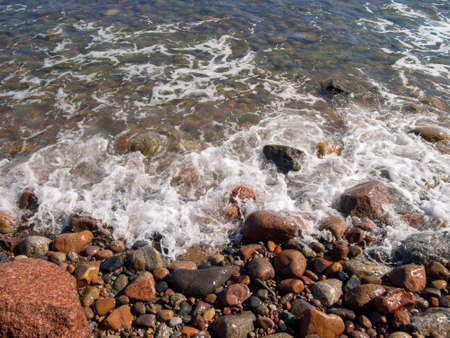 Waves hitting rocks on the beach and foaming. During sunny summer day from coast side looking to the seaの写真素材