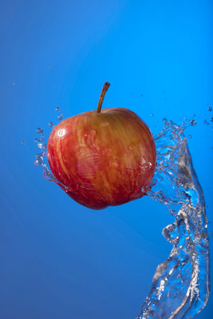 Delicious organic red apple fruit on blue background with water splash motion. Ideal for health...