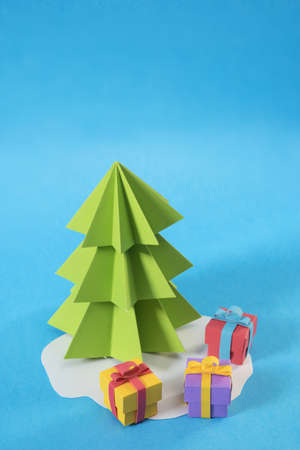 Christmas tree in paper cut handmade style with gift boxes on colorful blue background. Ideal for xmas greeting card, holiday poster or web.の写真素材