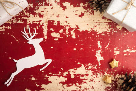 Vintage christmas time top view concept scene with copy space. Retro holiday decoration and paper cut reindeer silhouette on red grunge wood background.の写真素材