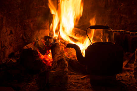 Kettle in fireplace, fire and wood burning. Cozy winter holiday cabin scene.の写真素材