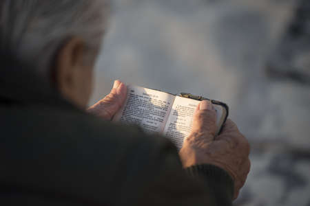 Elder man reading holy bible in spanish seen from over the shoulder angle view, religion concept.の写真素材
