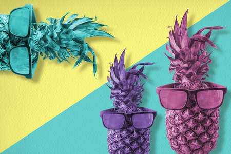 Cool pineapple fruits wearing hipster style sunglasses, trendy retro summer concept with colorful background design.の写真素材