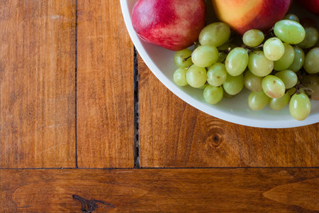 Fruit bowl with apple, peach and grapes shot from top view angle on wood texture background. Healthy organic food in wooden table, includes copy space.の写真素材