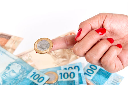 Woman's hand holding Brazilian coin and money to backgroundの写真素材