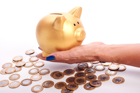 Woman's hand holding piggy bank and coins of the Brazilian money scattered on white background.の写真素材