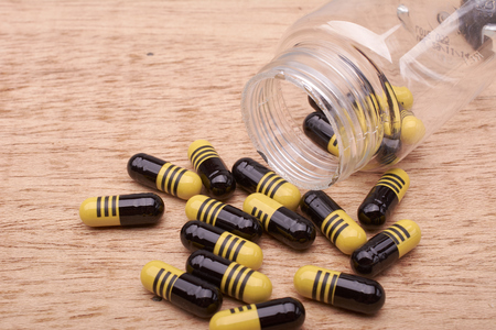 Capsules or pills yellow and black of medicament from transparent bottle on wood backgroundの写真素材