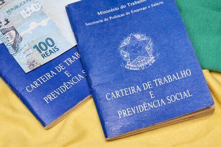 Brazilian work books or document work, social security or worker rights (Carteira de trabalho e Previdencia Social) on the Brazilian flag with money notes.の写真素材