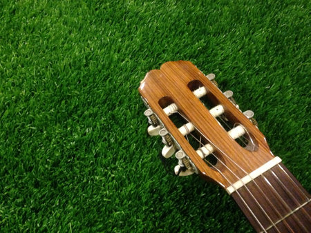 Close up photo of the head of an classical acoustic guitar on grassy ground.