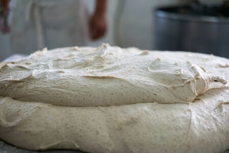 Lump of fresh multigrained bread dough with a blurred out baker standing in the background of the photo.の写真素材