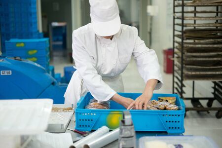 A Baker loading a tray of pastries with different types of baking equipment in the background. The baker is in full white baking uniform.の写真素材