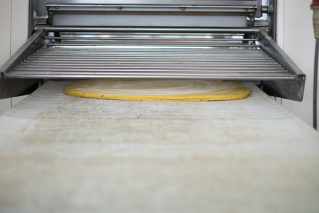 Pie crust being rolled out in a pastry dough rolling machine at a local bakery.の写真素材