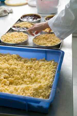Pastry chef toping off nearly finished cherry filled cheese cake pies with cookie crumble topping and graham crackers crust.の写真素材