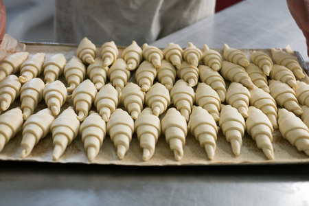 A baker picking up a tray of raw croissants dough taking it to the oven to be baked.の写真素材