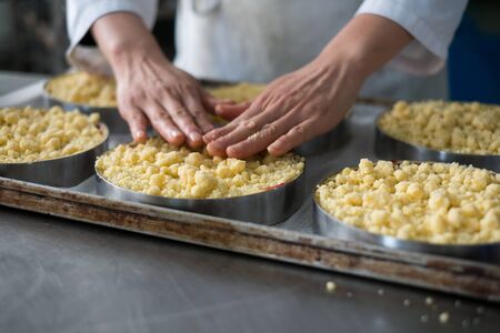 Pastry chef toping off nearly finished cherry filled cheese cake pies with cookie crumble topping and graham crackers crust.の写真素材