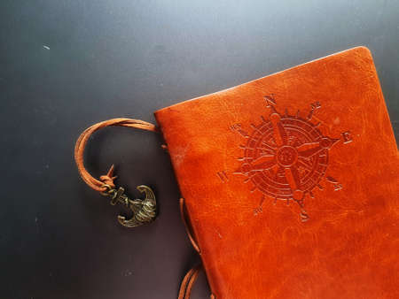 A notebook with a brown leather cover with a compass motif and anchor strap.の写真素材