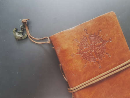 A notebook with a brown leather cover with a compass motif and anchor strap.の写真素材