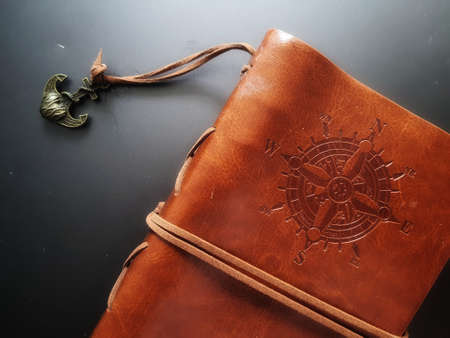 A notebook with a brown leather cover with a compass motif and anchor strap.の写真素材