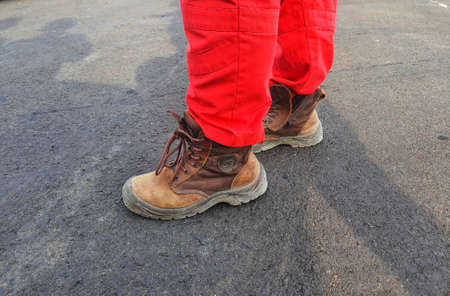 The lower of the feet of a healthy safety and environmental officer who wears a red uniform (pants) and brown safety shoes.の写真素材