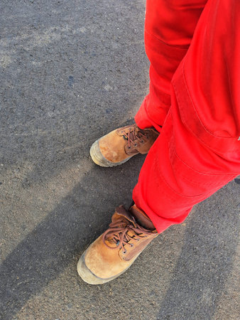 The lower of the feet of a healthy safety and environmental officer who wears a red uniform (pants) and brown safety shoes.の写真素材