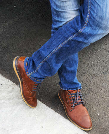The lower of the legs of a standing man wearing blue denim jeans with brown leather shoes.の写真素材