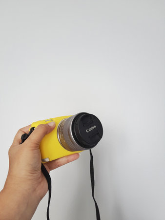 West Java in August 2022. A hand is holding a canon eos m10 camera, this camera is given a yellow rubber protector.のeditorial素材