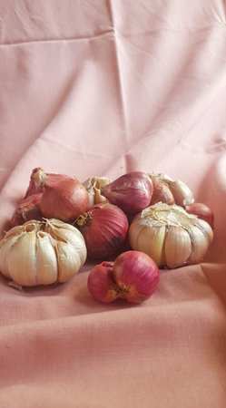 This is a photo of some cloves of garlic and onion or shallots placed on a pink cloth.の写真素材