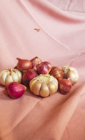 This is a photo of some cloves of garlic and onion or shallots placed on a pink cloth.の写真素材