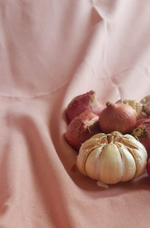 This is a photo of some cloves of garlic and onion or shallots placed on a pink cloth.の写真素材