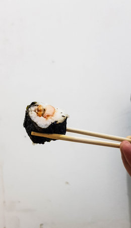 A piece of sushi held with chopsticks. With a white wall background.の写真素材