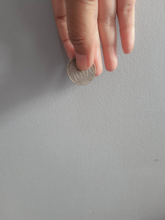 Isolated photo of a hand holding a thousand rupiah coin. This coin is usually used to pay for the averse or parking attendant or given to beggars or charity.の写真素材