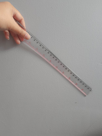A hand is holding a plastic ruler. This ruler is short, only thirty centimeters long.の写真素材