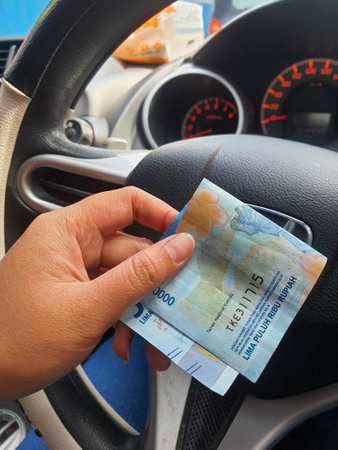 A hand is holding a fifty thousand rupiah bill which bends while driving. This money will be given to pay for cash parking.の写真素材